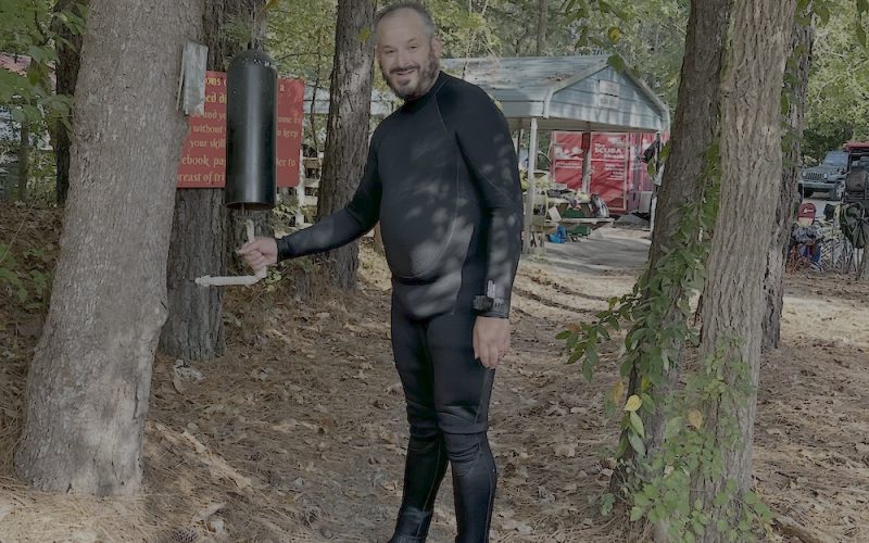 A scuba student in wetsuit rings the certification bell at Lake Phoenix.