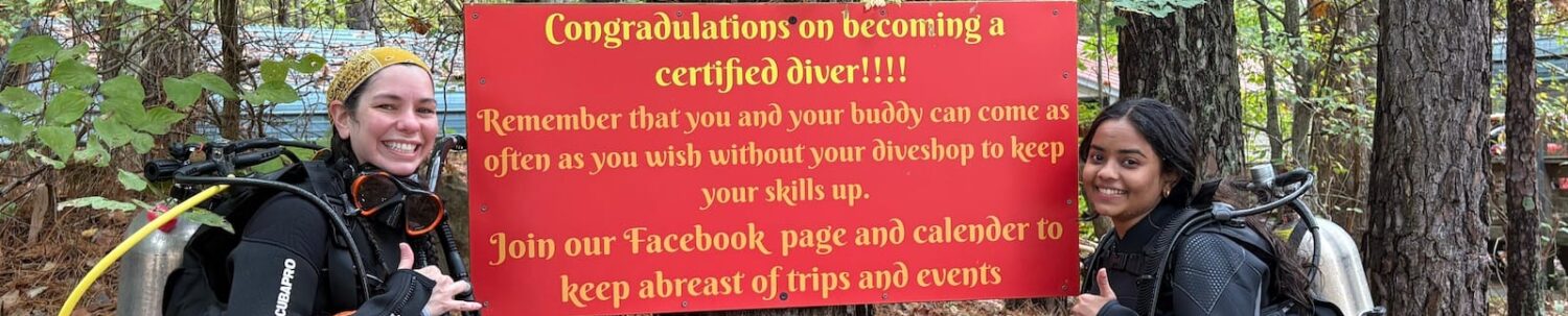 Scuba student celebrating certification at Lake Phoenix congratulatory sign.