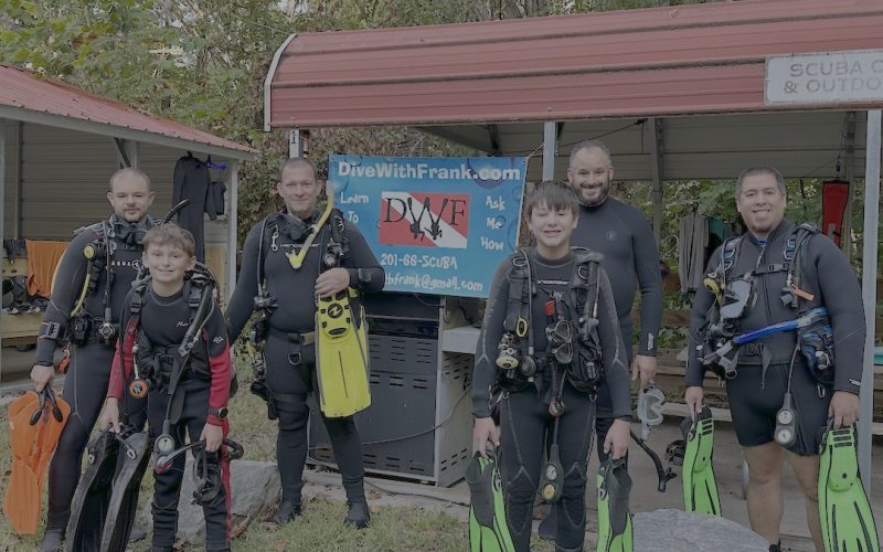 Group of new scuba divers with instructors standing in front of DiveWithFrank sign at Lake Phoenix