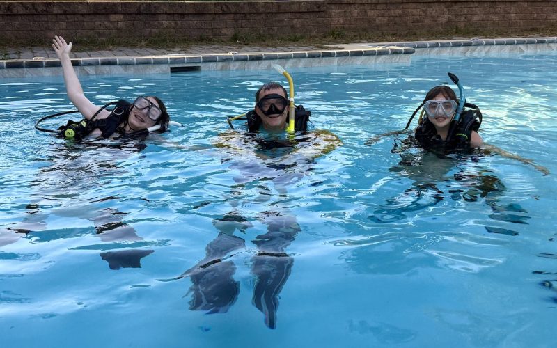 Two young scuba students smiling in the pool during their final confined water dive session.