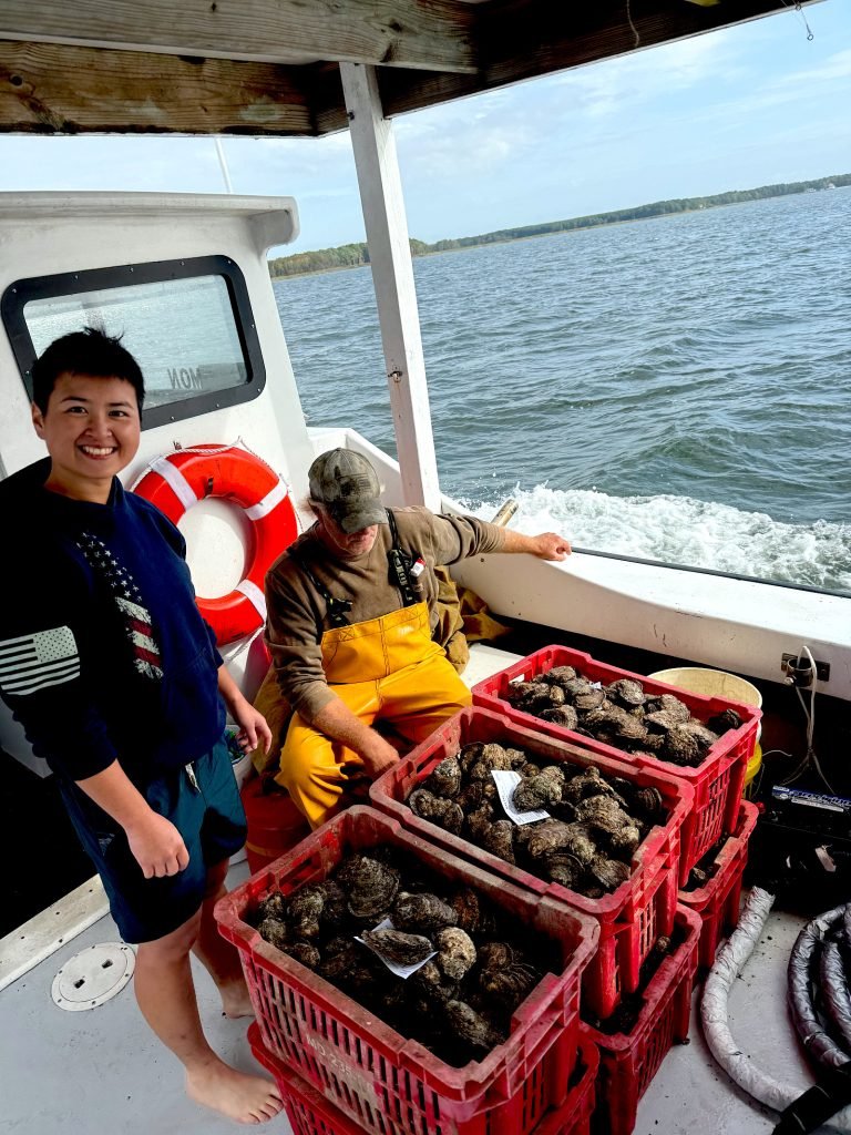 Diver and first mate beside stacked red crates full of harvested oysters.