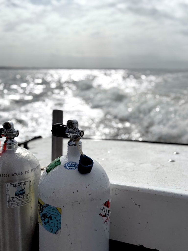 Two scuba tanks on a boat rail with sunlight glinting off the water.