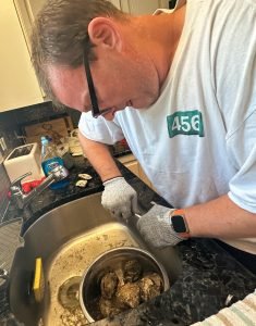 DWF shucking oysters over a kitchen sink with gloves on.