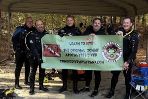 Group of divers holding the Zombie Apocalypse Diver banner under the DWF Basecamp shelter at Lake Phoenix.