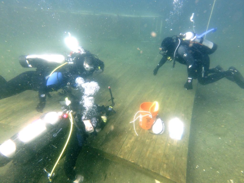 Team of divers working together underwater around a platform with buckets and gear.