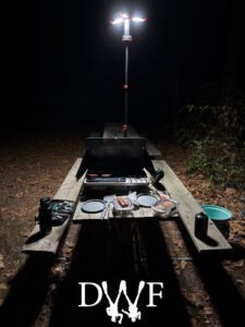 Camping stove and food setup under a tall lantern at night