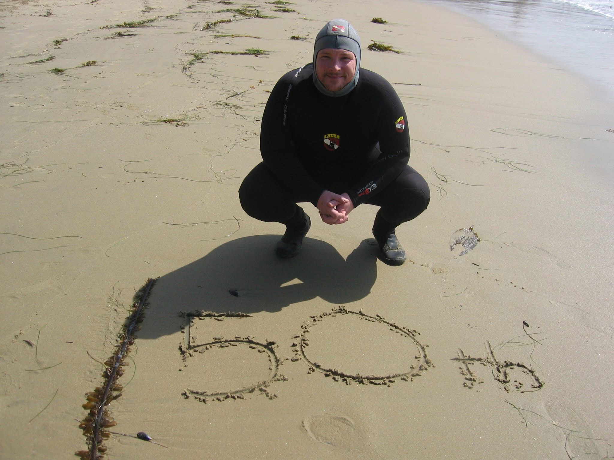 Scuba diver celebrating a fiftieth dive milestone on a Southern California beach.