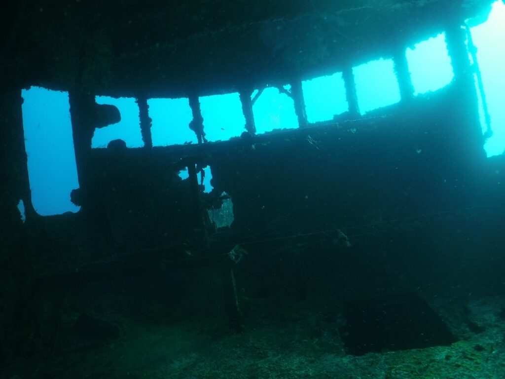 Dark interior of a sunken wreck with blue water visible through the wreck windows