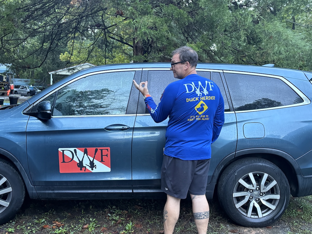 Dive With Frank instructor wearing blue Duck Herder long sleeve shirt next to branded blue SUV
